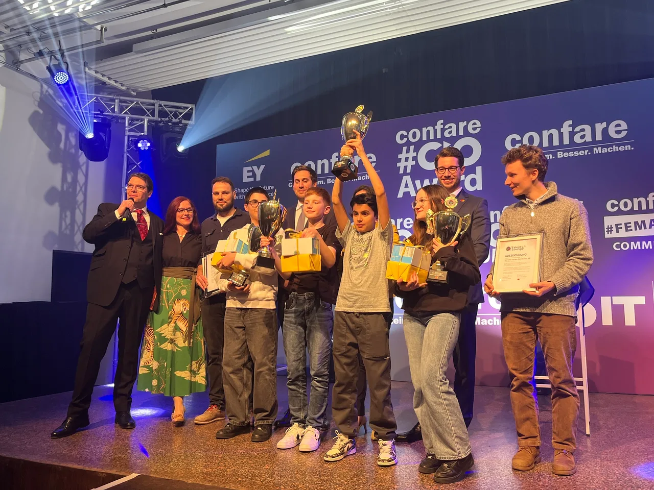 Ausgezeichnete Schüler:innen auf der Bühne des Confare #CIOAWARD, ein Pokal wird in die Höhe gehalten