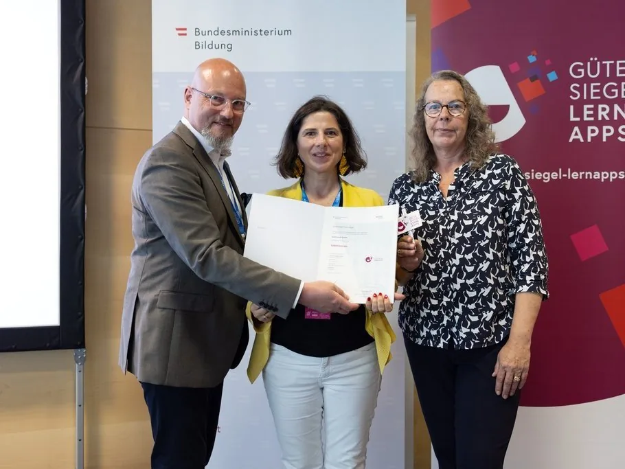 Übergabe der Urkunde für das Gütesiegel Lern-Apps an die TalentsLounge - drei Personen halten die Urkunde vor den Bannern des Bildungsministeriums und des Gütesiegels